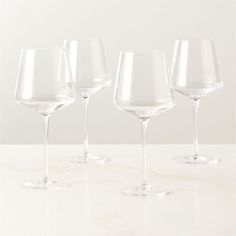 four empty wine glasses lined up on a white counter top, with one in the foreground