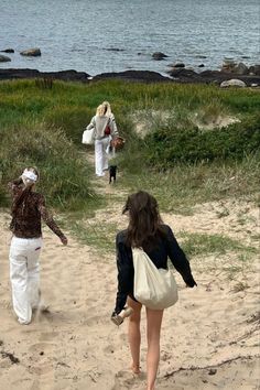 two women walking on the beach with one carrying a bag and another carrying a purse