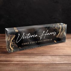 a black and gold business card holder on top of a wooden table with the name victoria harris