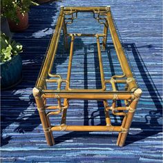 a bamboo table with glass top sitting on a blue rug next to potted plants