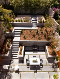 an aerial view of a patio and dining area in a backyard with stone walls, grass roofing and stairs leading up to the upper level