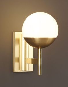 a wall light with a white ball on it's arm and a gold finish