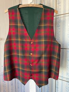 This striking vest is made from a lightweight wool blend in classic tartan in red, dark green and harvest gold. It buttons in the front and is partially lined with dark red silky lining. The back is made of a fine knit in dark green. The measurements, taken with the vest lying flat, are: shoulder to shoulder, 13 1/2 inches; armpit to armpit, 20 1/2 inches; length 25 1/2 inches (front) and 22 inches (back); bottom edge, 20 inches. Please note that the back has a few small holes; otherwise, the vest is in very good condition. Classic Green Vest For Winter, Classic Green Winter Vest, Plaid Vest For Fall, Plaid Sleeveless Vest For Fall, Classic Plaid Vest For Fall, Classic Plaid Vest, Classic Plaid Sleeveless Vest, Classic Red Vest For Fall, Classic Sleeveless Plaid Vest