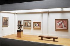 an art gallery with paintings on the wall and wooden bench in front of it,