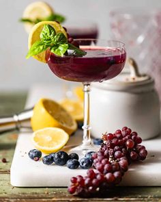 a glass filled with red wine and garnished with lemons, blueberries and mint