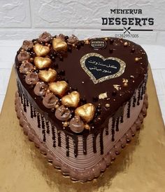 a heart shaped chocolate cake with gold hearts on the top, and words desserts written in arabic