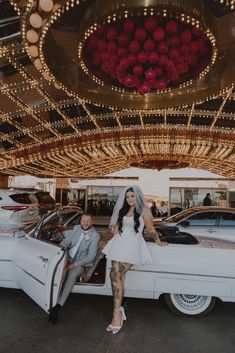 a bride and groom pose in front of their wedding car at the fairground for a photo