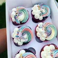 six cupcakes in a box decorated with rainbow icing