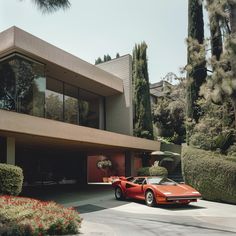 a red sports car parked in front of a large house with trees and bushes around it