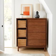 a wooden dresser with baskets on top of it next to a white wall and stairs