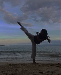 a woman doing a yoga pose on the beach in front of the ocean at sunset