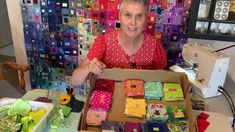 a woman in a red shirt is holding a box full of quilts and fabrics