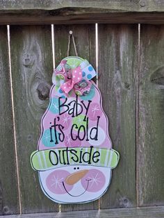 a sign that says baby it's cold outside hanging on a wooden fence with a pink bow