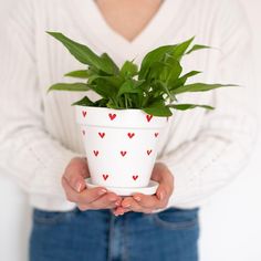 a woman holding a potted plant with hearts painted on it