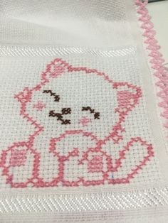 a cross - stitch hello kitty is shown on a piece of white fabric with pink trim