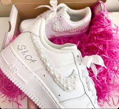 a pair of white sneakers with pearls on them sitting in a box filled with pink shredded grass