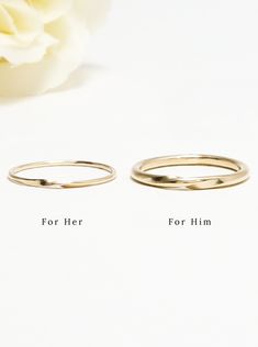 two gold wedding rings sitting next to each other on top of a white table with a flower