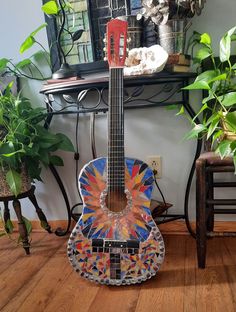 a colorful guitar sitting on top of a wooden floor next to a potted plant