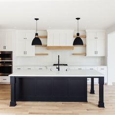 a large kitchen with an island in the middle and two pendant lights hanging over it