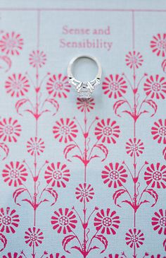 a silver ring sitting on top of a red and white flowered table cloth next to a card