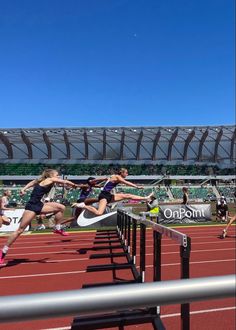 two women jumping over a hurdle on a race track in front of an empty stadium