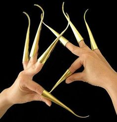 two hands holding gold colored metal objects in the shape of claws, with black background