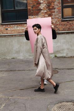 a woman holding a pink piece of paper in her hands and walking down the street