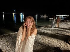 a woman talking on a cell phone while standing next to the ocean with boats in the background