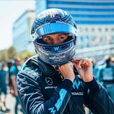 a man wearing a racing helmet and holding his hand up to his face while standing in front of a crowd