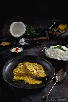 some food is sitting on a table with spoons and rice in bowls next to it