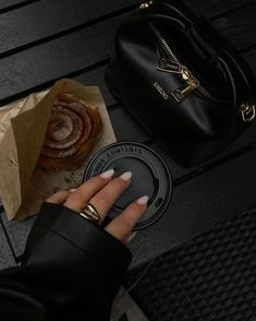 a woman's hand on a coffee cup next to a black purse and pastry