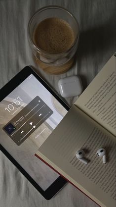 an open book sitting on top of a bed next to headphones and a cup of coffee