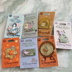 six disney pin's are sitting on a marble counter top, each with different designs and colors