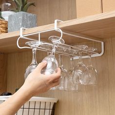 a person holding a wine glass in front of a shelf filled with glasses on it