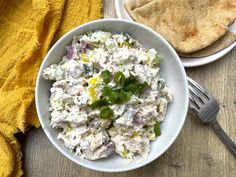 a white bowl filled with food next to a plate of pita bread on top of a wooden table