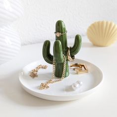 a small green cactus sitting on top of a white plate next to pearls and a shell