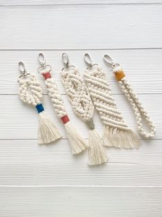 four macrame key chains with tassels hanging from them on a white wooden background