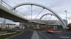 a large bridge over a street with traffic passing by on both sides and buildings in the background