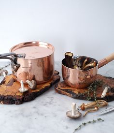 two pots and pans sitting on top of a wooden cutting board next to mushrooms