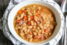 a white bowl filled with beans and carrots on top of a cloth next to a spoon