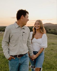 a man and woman standing in the grass holding hands