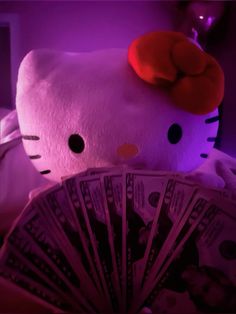 a hello kitty stuffed animal sitting on top of a pile of money with purple light behind it