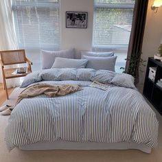 a bed with blue and white striped comforter next to a window in a bedroom