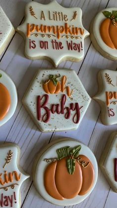 decorated cookies with words and pumpkins are arranged on a white wooden surface, including one that says'a little pumpkin is on the way '