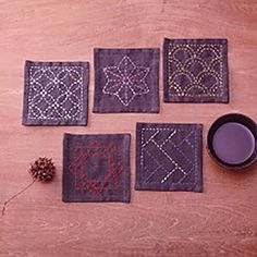 four square coasters with embroidered designs on them and a pine cone next to it