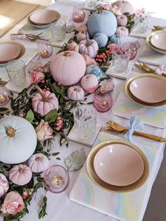 the table is set with pink and blue pumpkins, gold chargers, white plates, and silverware