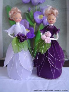 two dolls standing next to each other in front of some purple and white flowers on a table