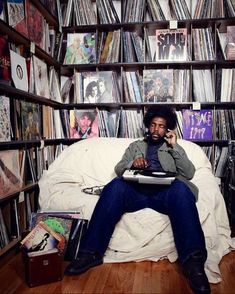 a man sitting on top of a bed next to a book shelf filled with records