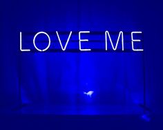 a neon sign that says love me in front of a dark blue background with curtains