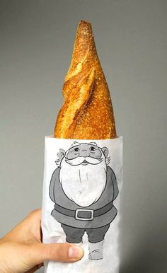 a hand holding a baguette wrapped in paper with an image of santa claus on it